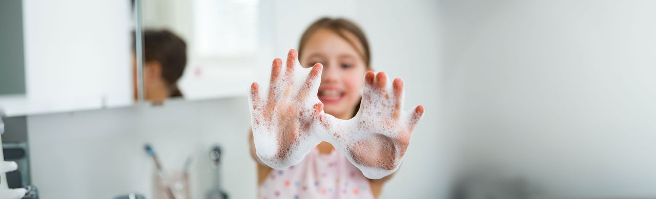 A young, smiling child showing her hands covered in soap suds. 