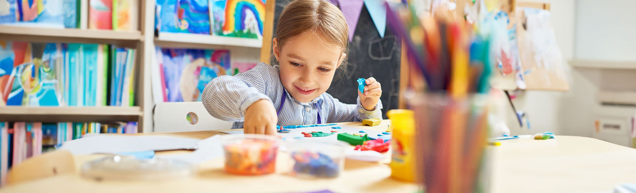 A smiling child working with plasticine in arts and crafts class.