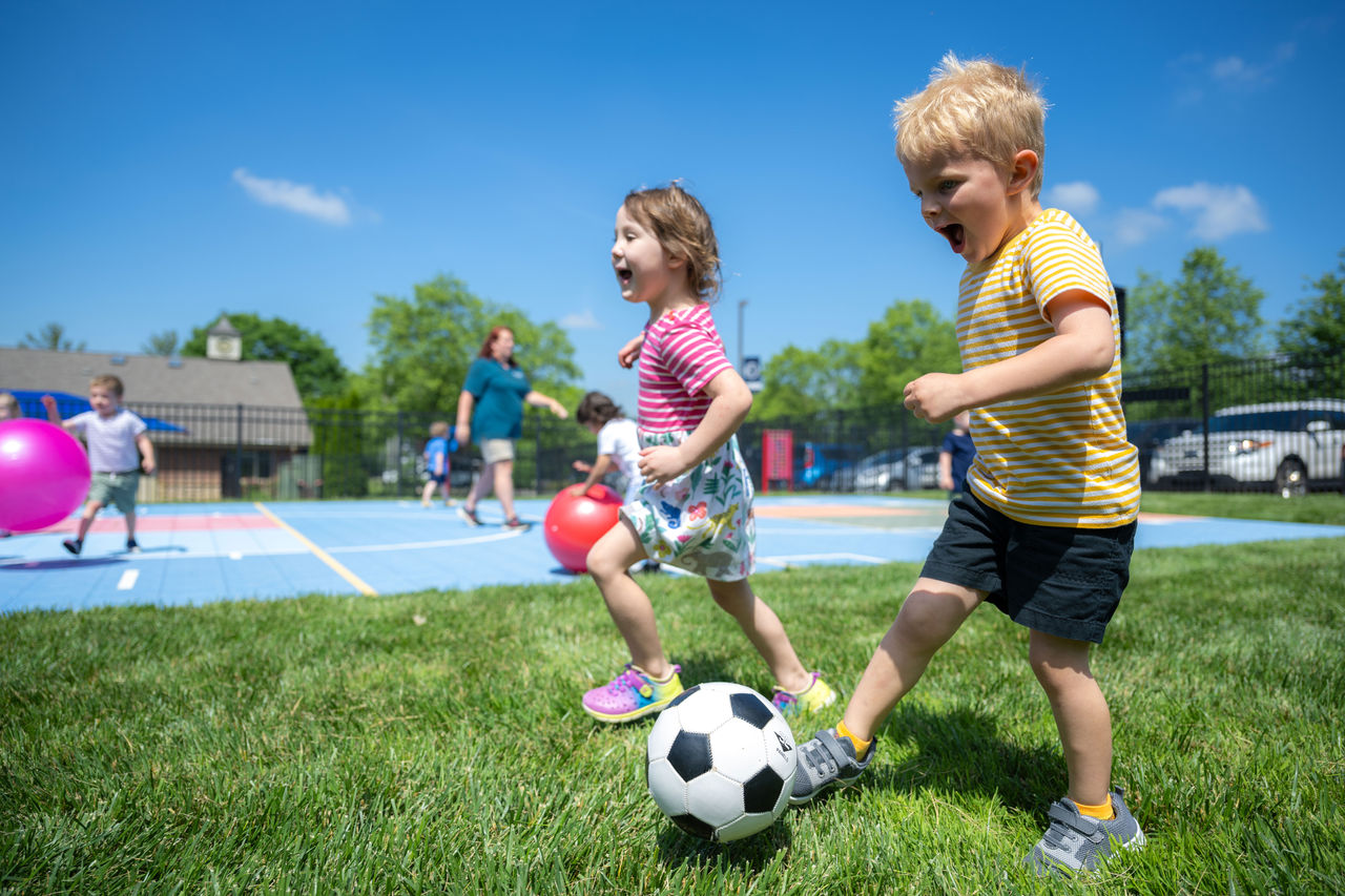 Two happy children running and playing soccer on a preschool playground