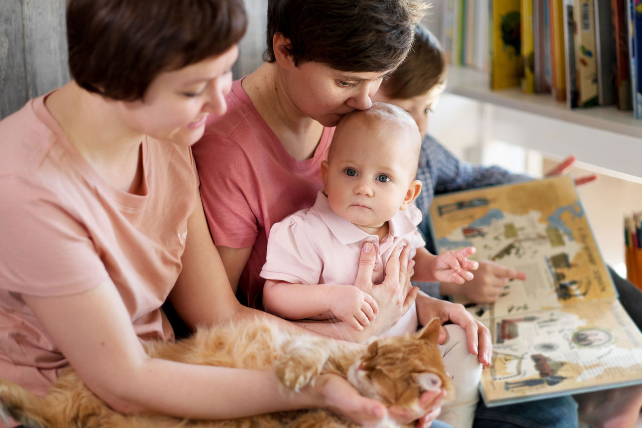 Women sitting with a baby, cat and boy looking at a book