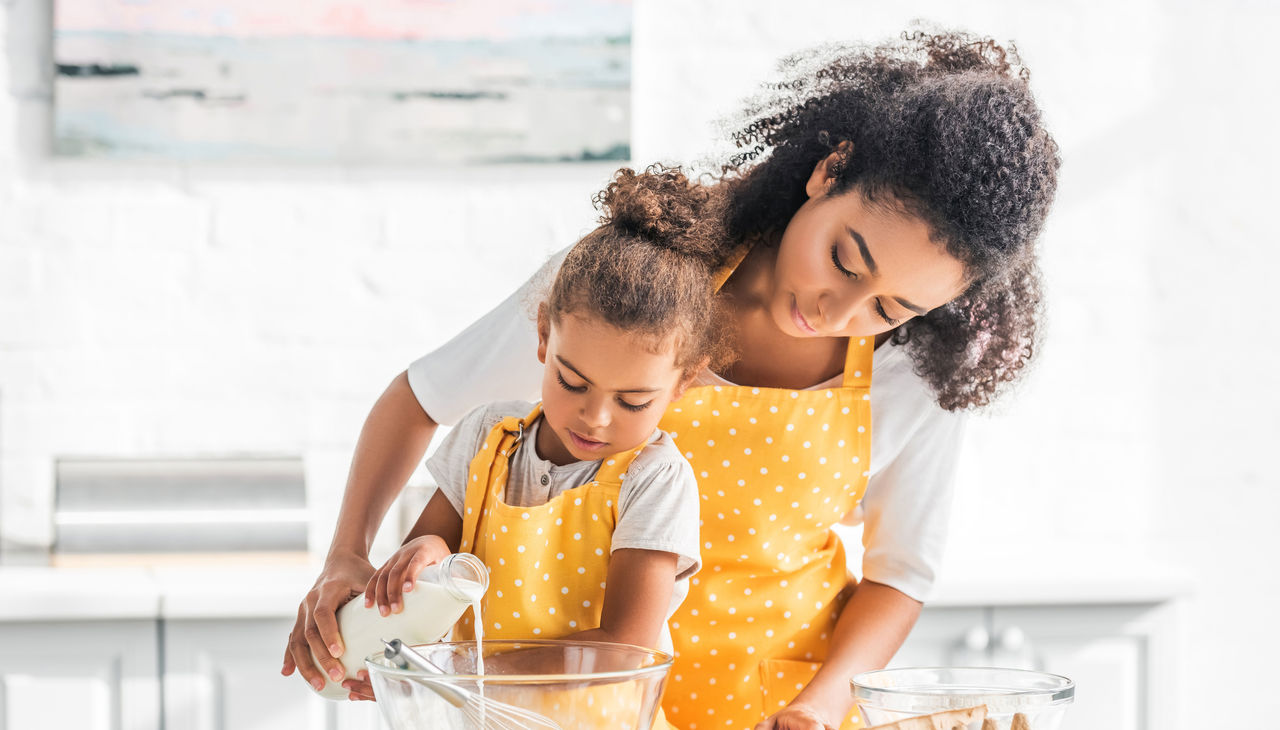 A mother and daughter in matching yellow aprons pouring milk into a bowl