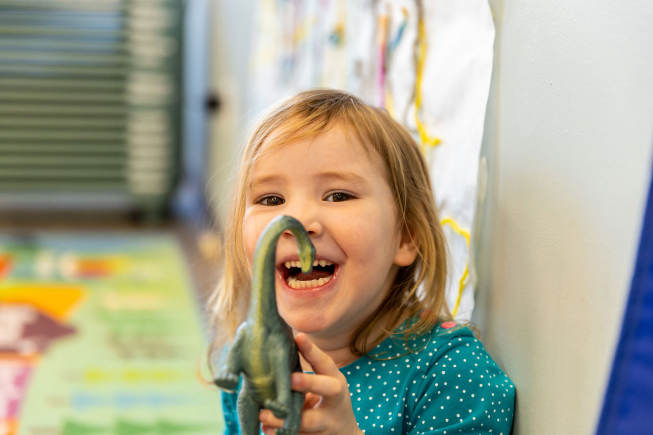 A young girl smiling and holding a toy dinosaur