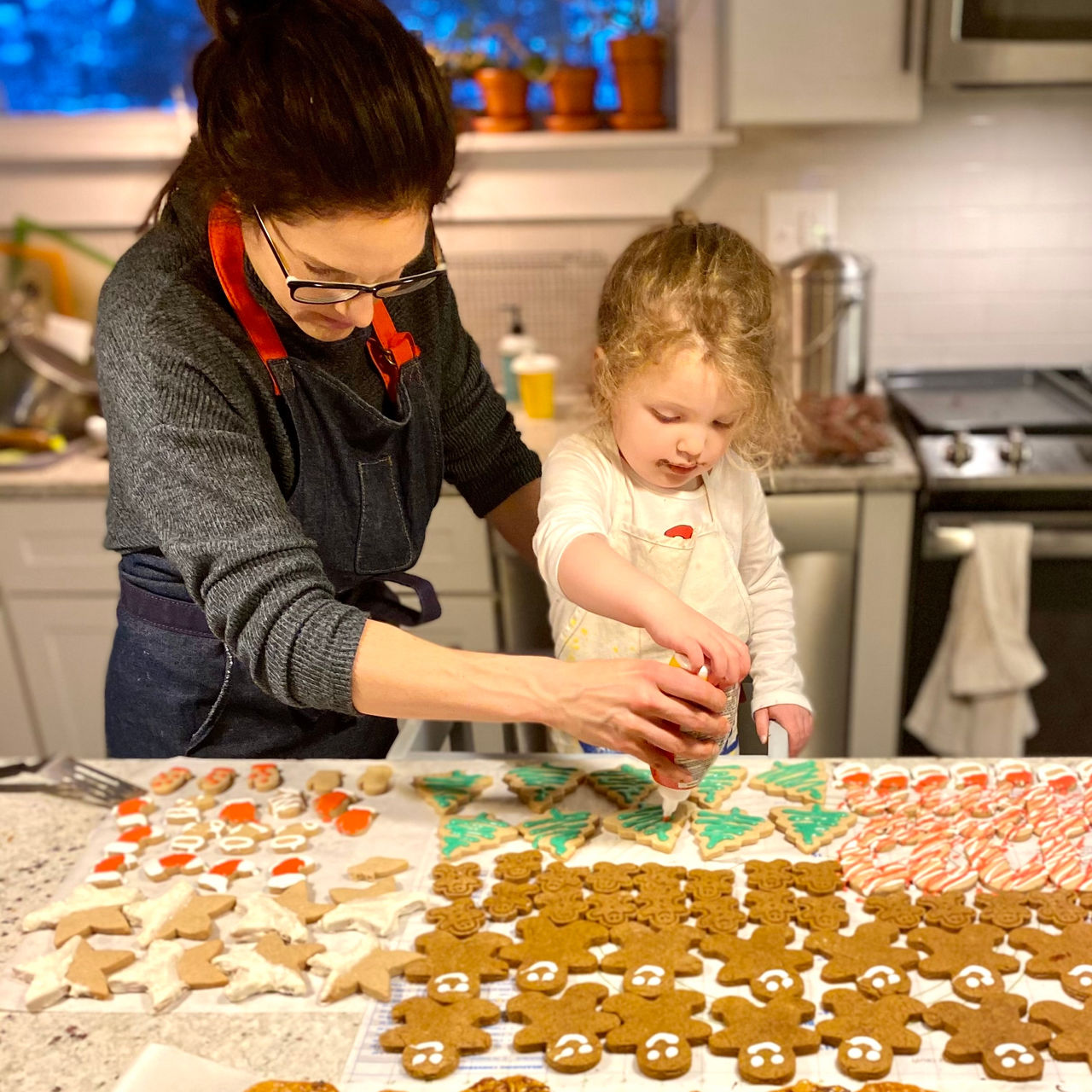 a mother and daughter in the kitchen decorating holiday cookies with icing
