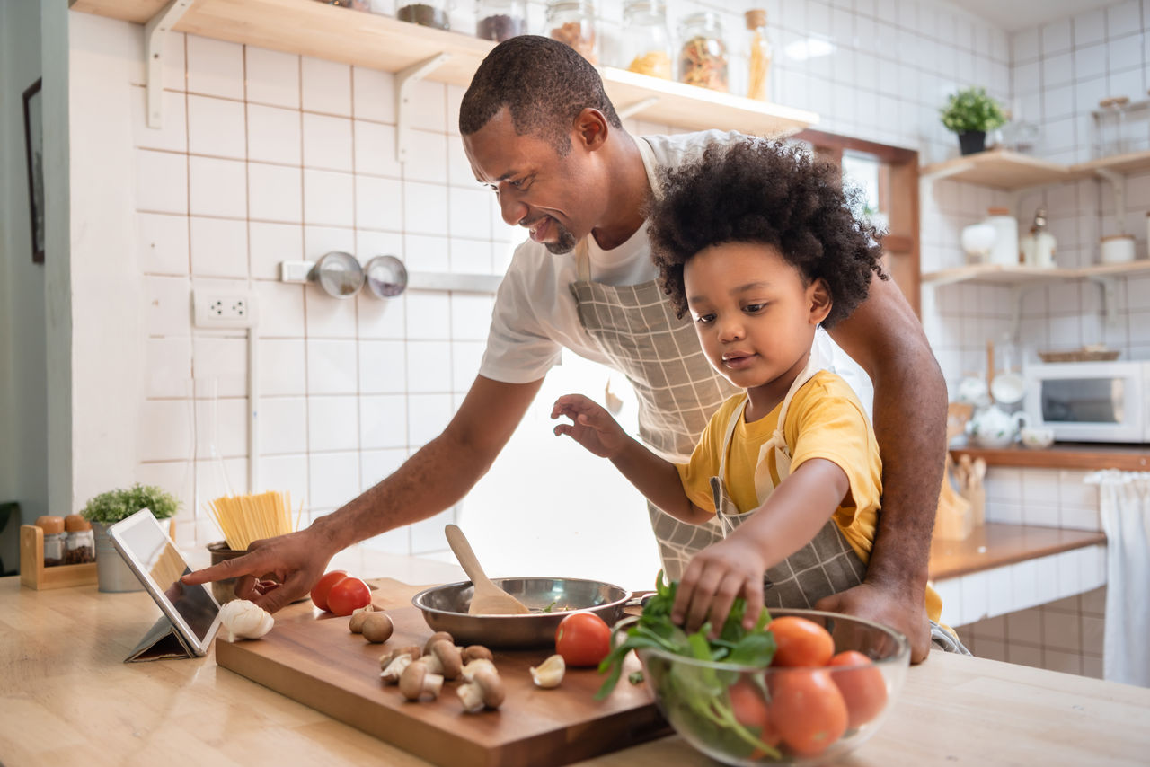 A father and daughter cooking together at an island in the kitchen with vegetables and pasta