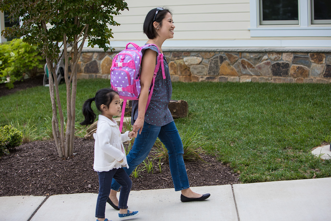 Mother and preschool child hold hands walking into school