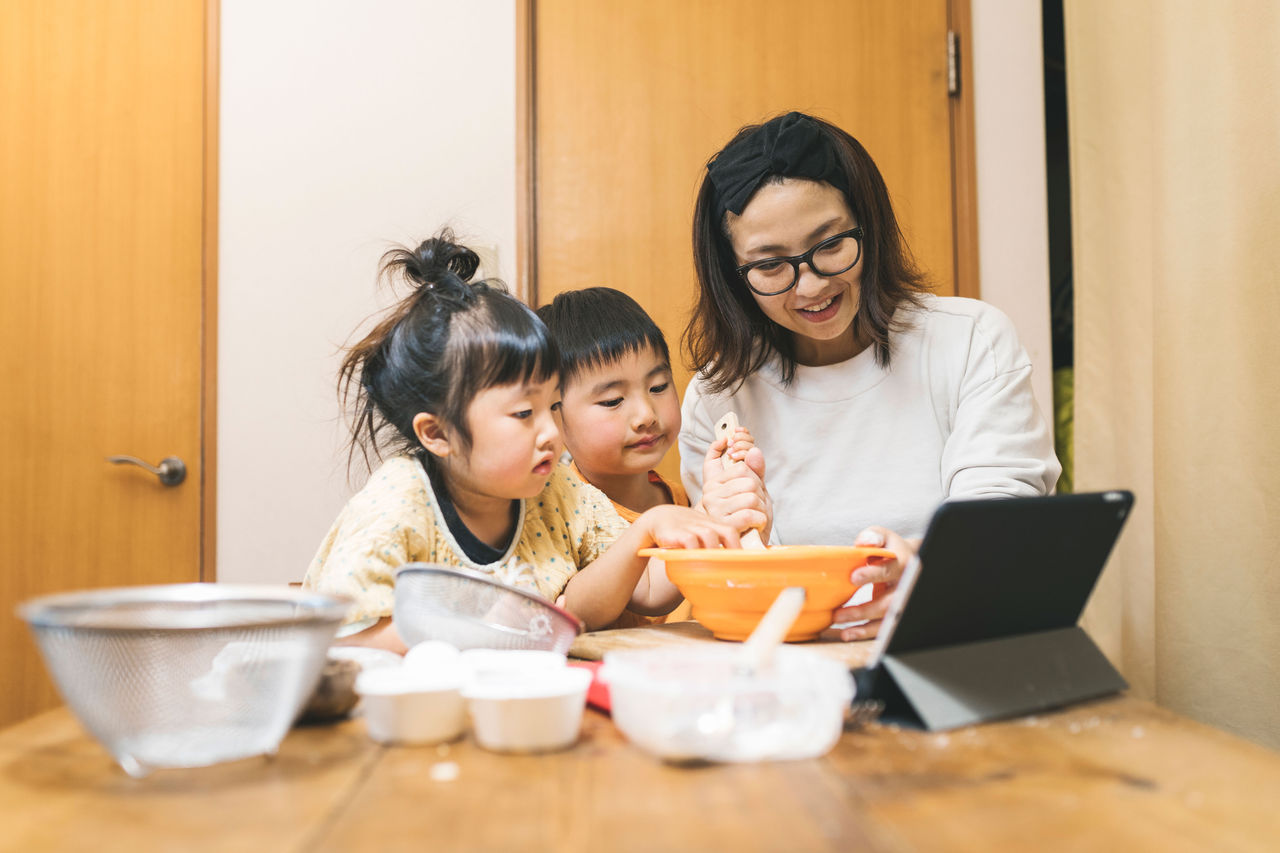 Mother and two children read a recipe and bake together