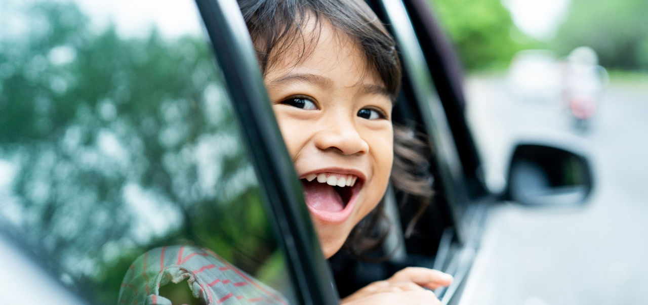 A smiling girl looking out a car window