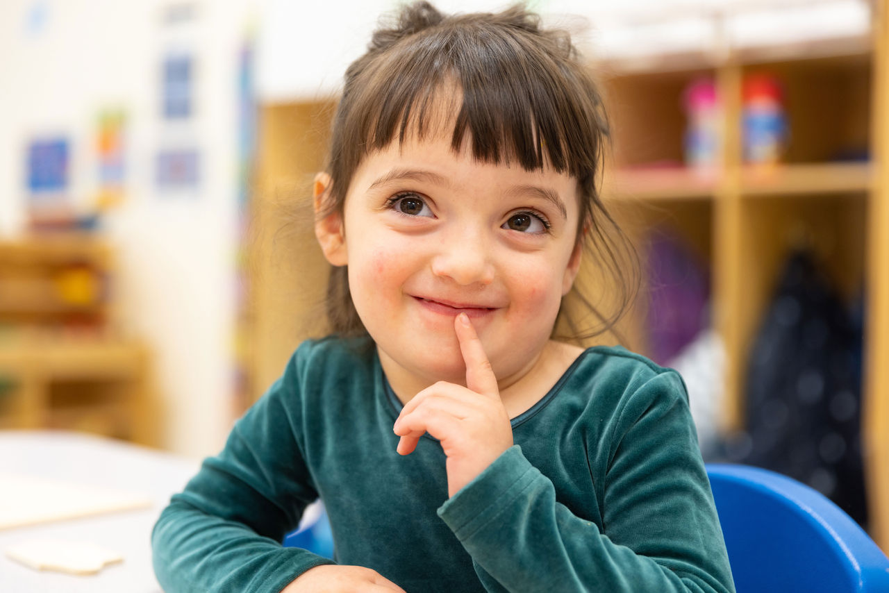 A young girl with a sly look on her face holding her finger up to her lips