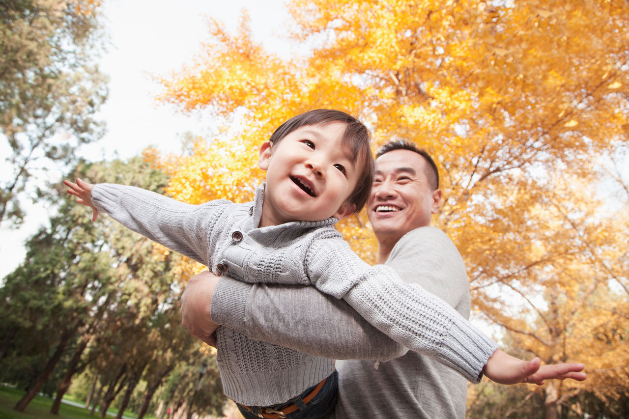 Dad flying son in arms under fall trees