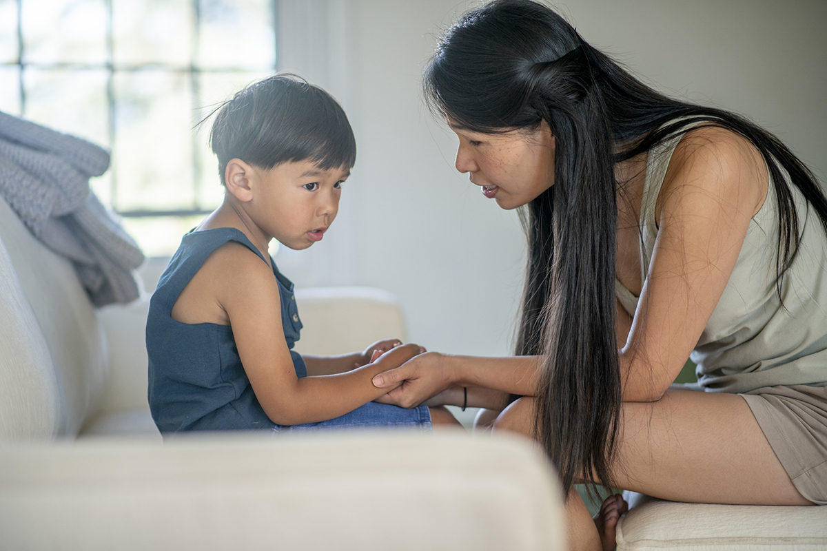 Preschool-aged child sitting on a couch holding hands with an adult in a calm home environment, emphasizing early childhood care and supportive interaction.