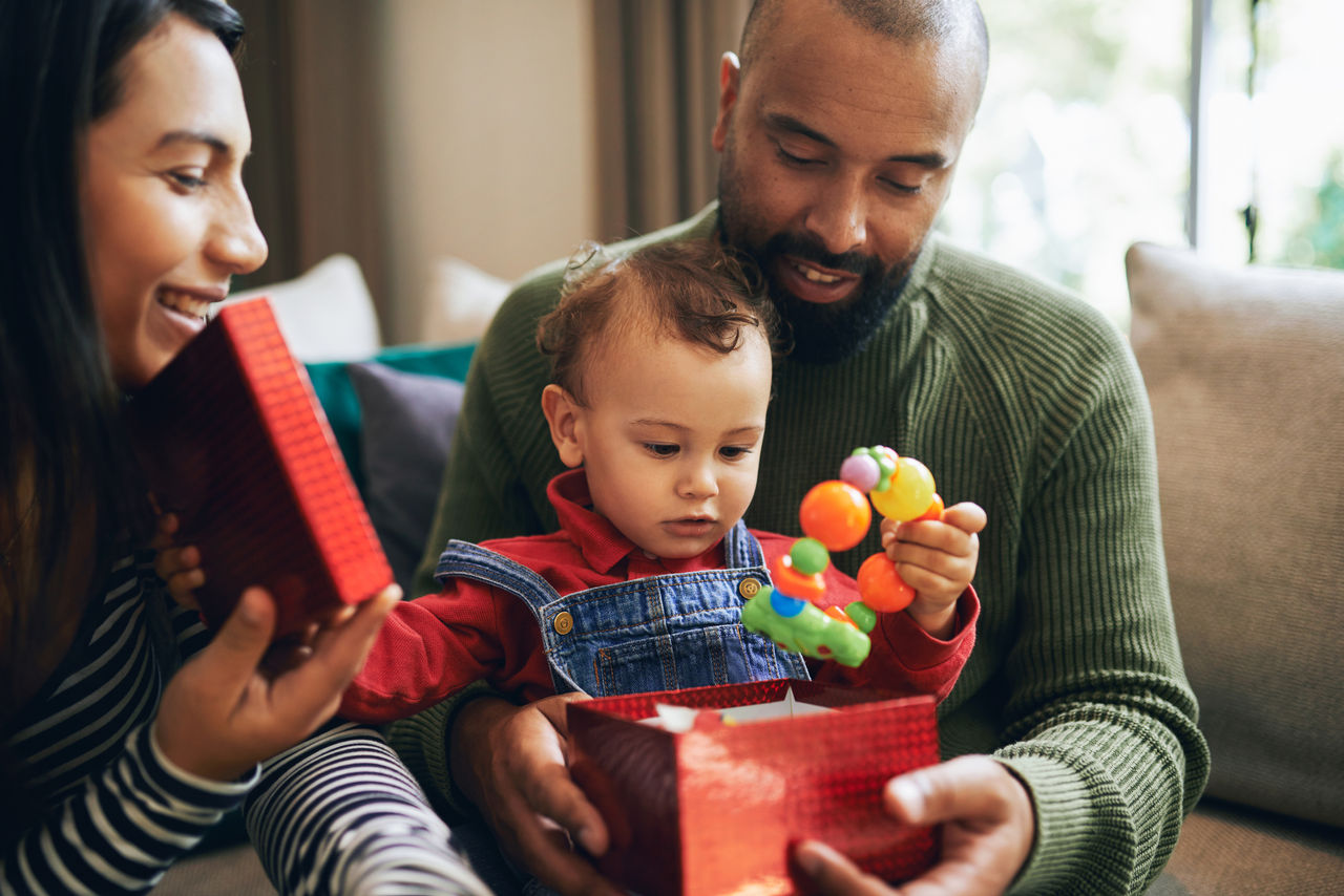 mother and father holding young child opening gift