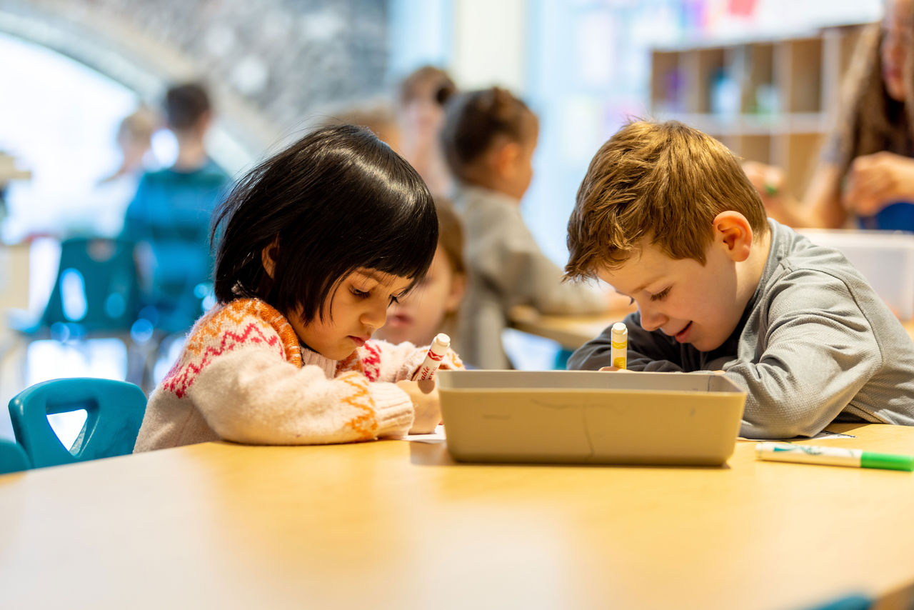 two children writing with markers at a classroom table