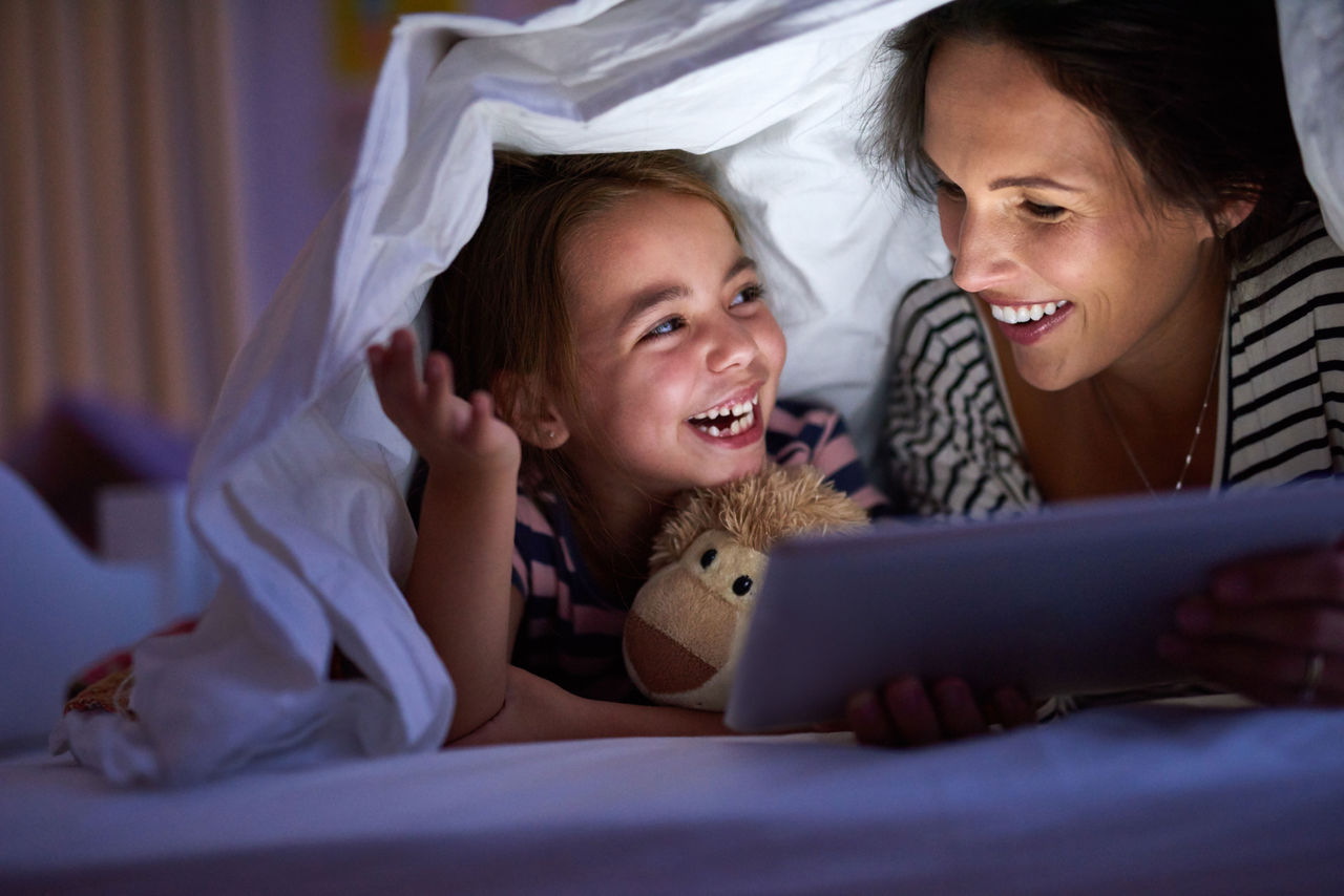 Mother and daughter looking at tablet while under a blanket
