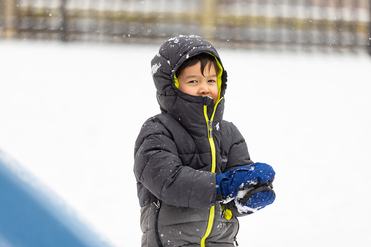 Preschool child dressed in a winter coat and gloves playing outside in the snow during outdoor winter activities.