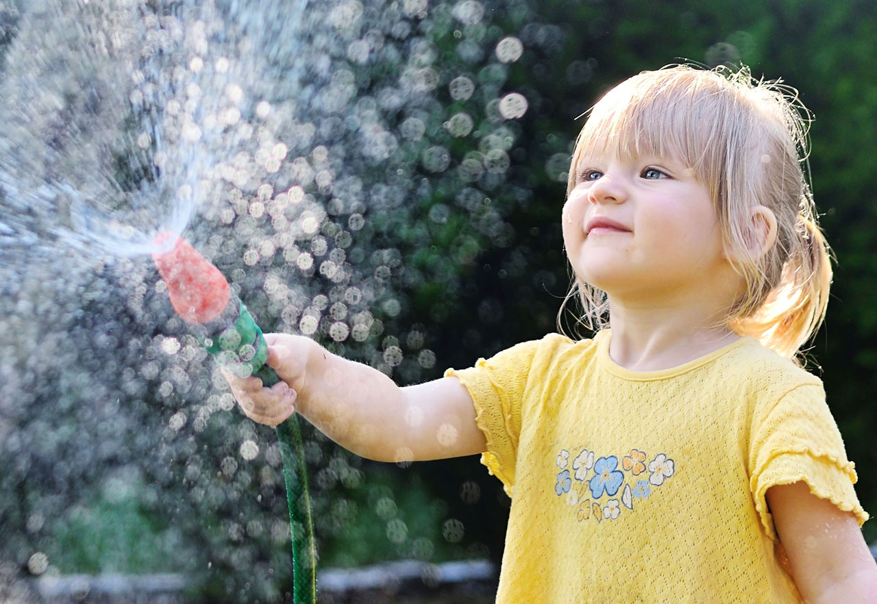 Child spraying a hose outdoors