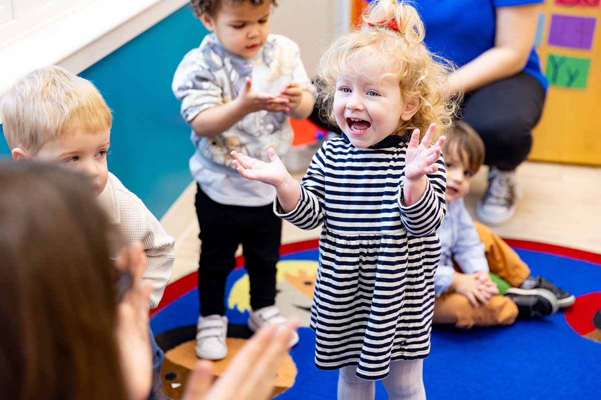 Preschool students clapping and engaging in a group learning activity during circle time in a bright classroom.