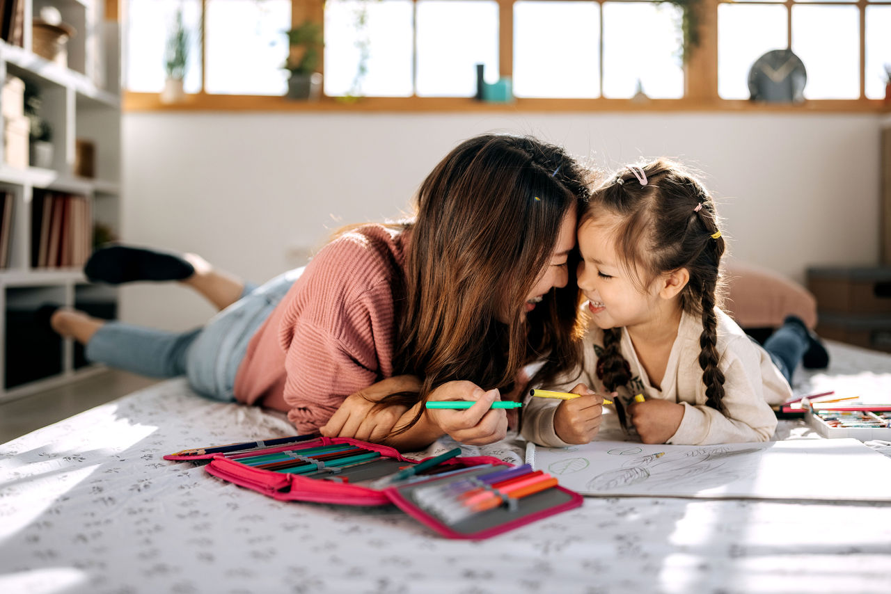 A mother and daughter smiling and coloring on the floor
