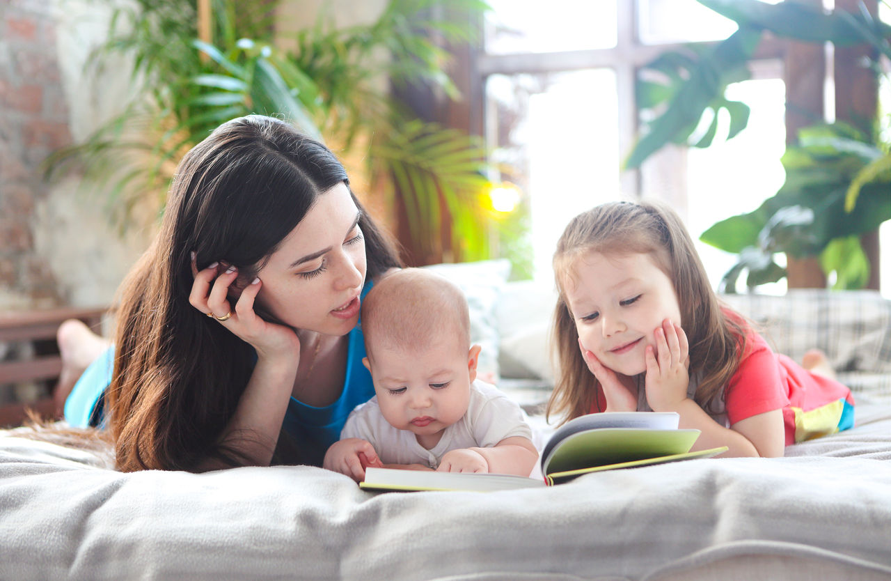 Young mother reading a book with her daughter and son in bedroom