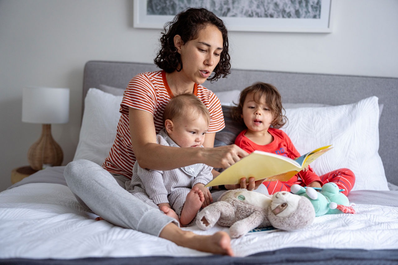 Mother reading to two a baby and toddler on a bed