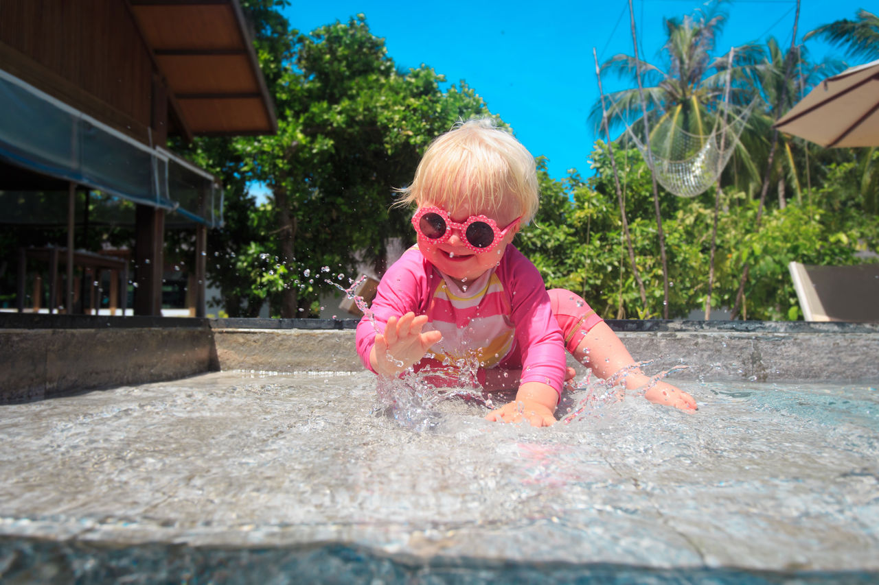 Baby in sunglasses splashing in water