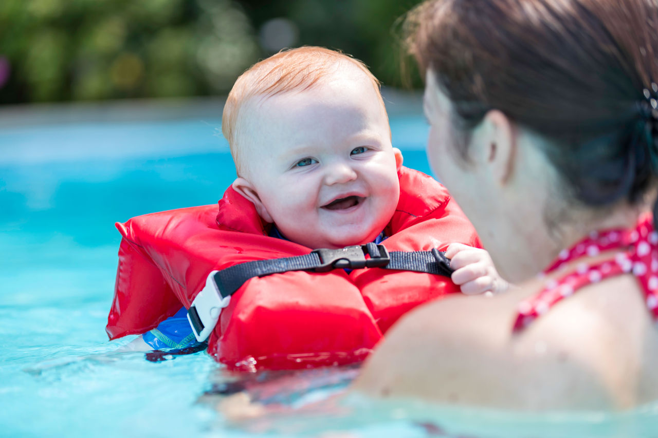 Baby wearing life jacket held by mother in pool