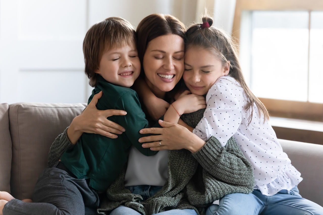 A boy and girl hugging their mother on a couch