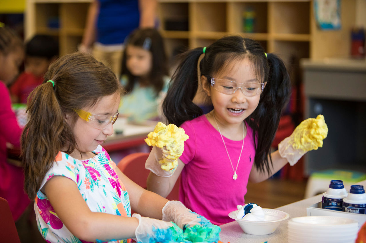 Two young girls wearing gloves doing a science experiment in a classroom