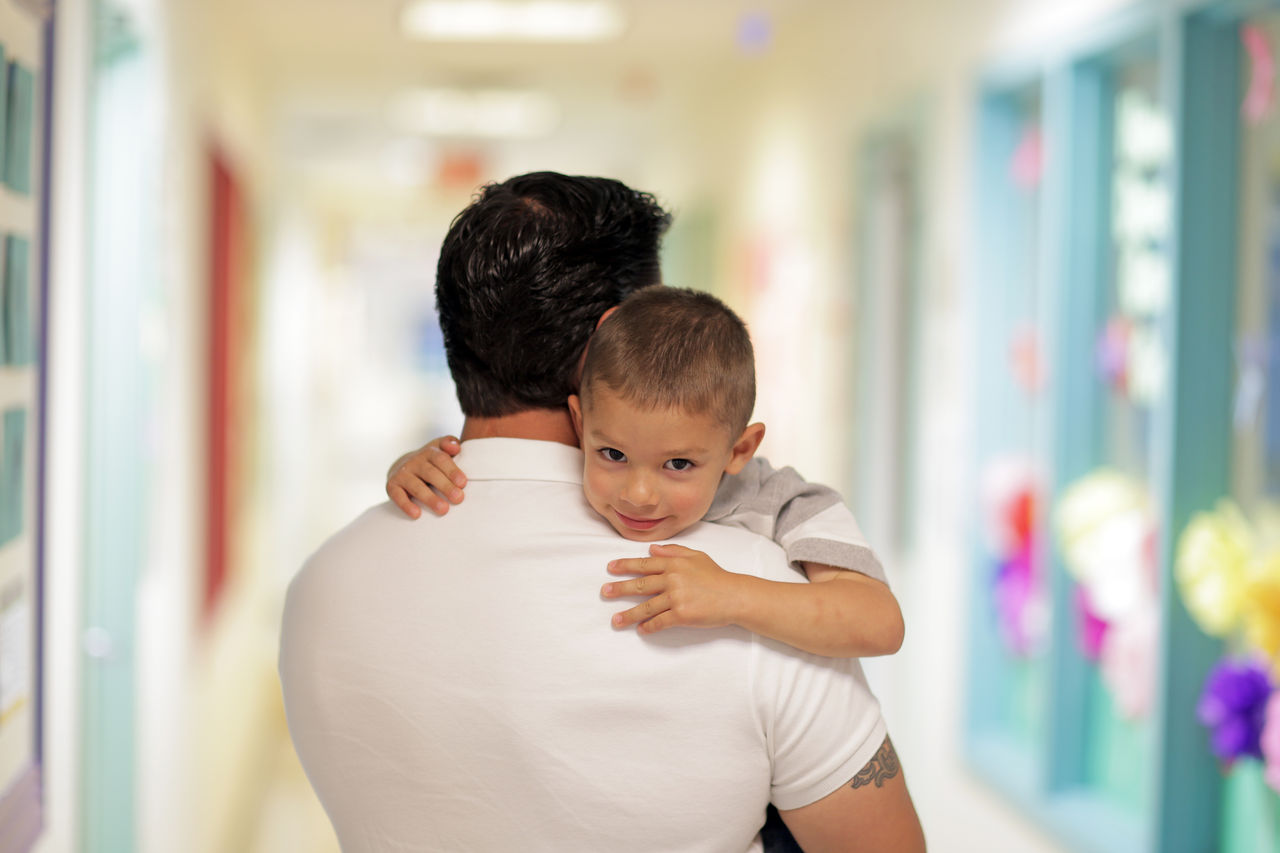 Preschool child hugs parent while being carried into school