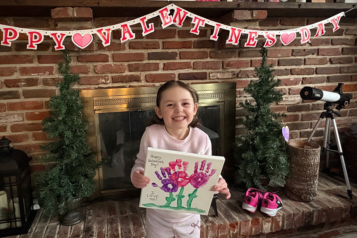 Preschool Valentine’s Day handprint craft held by a child in a cozy indoor setting with festive Valentine decorations.