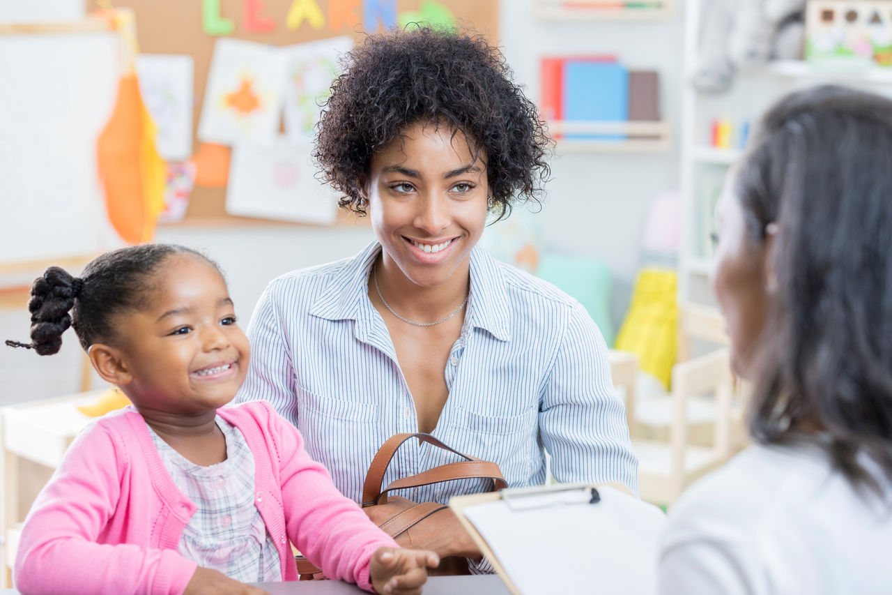 A mother and daughter smiling and talking with a teacher in a classroom