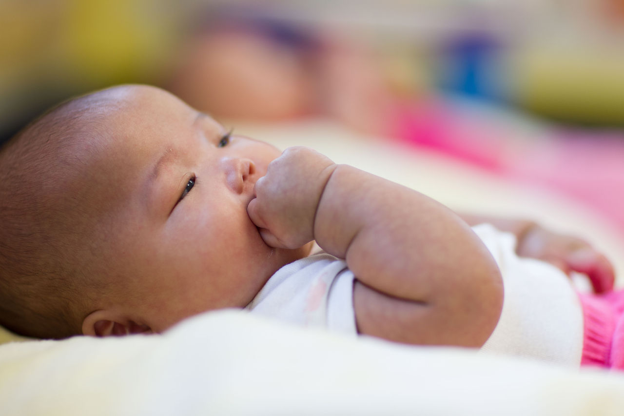 A baby sucking their fist while lying on their back