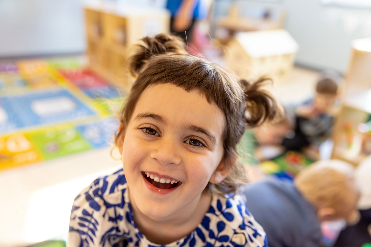 Small child with hair in pigtails smiling in a classroom