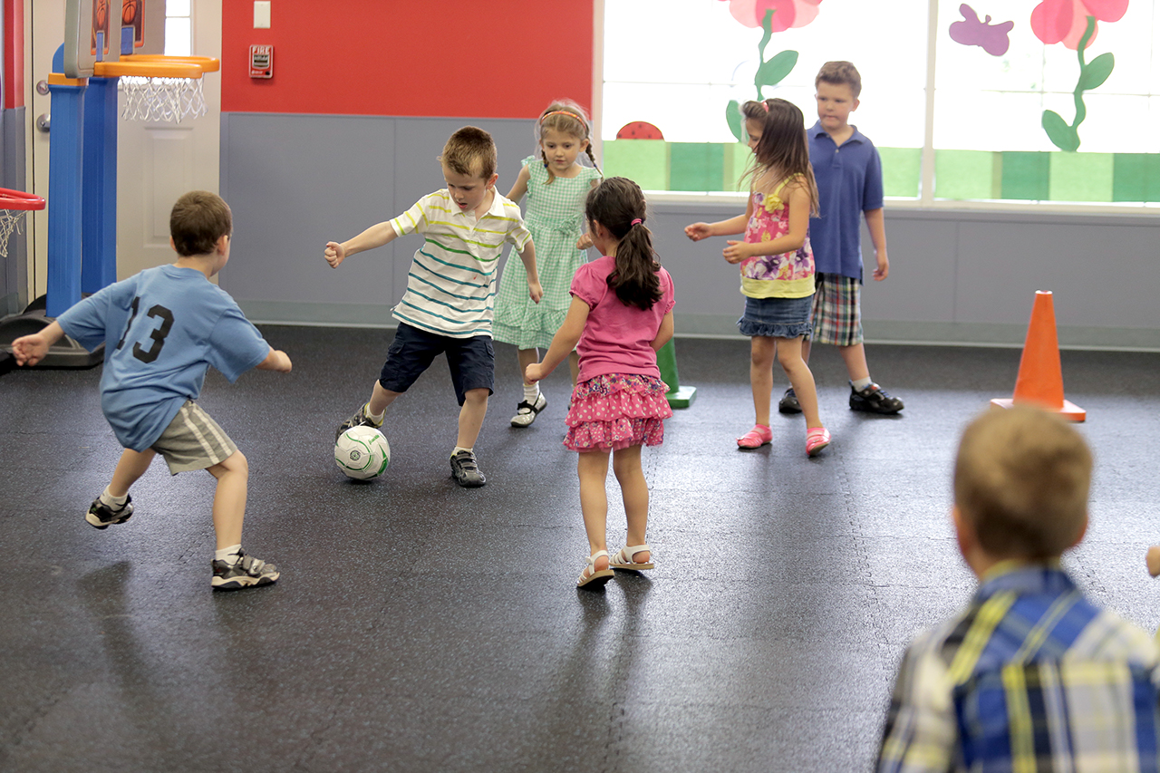 A group of older children play soccer in an indoor play space.