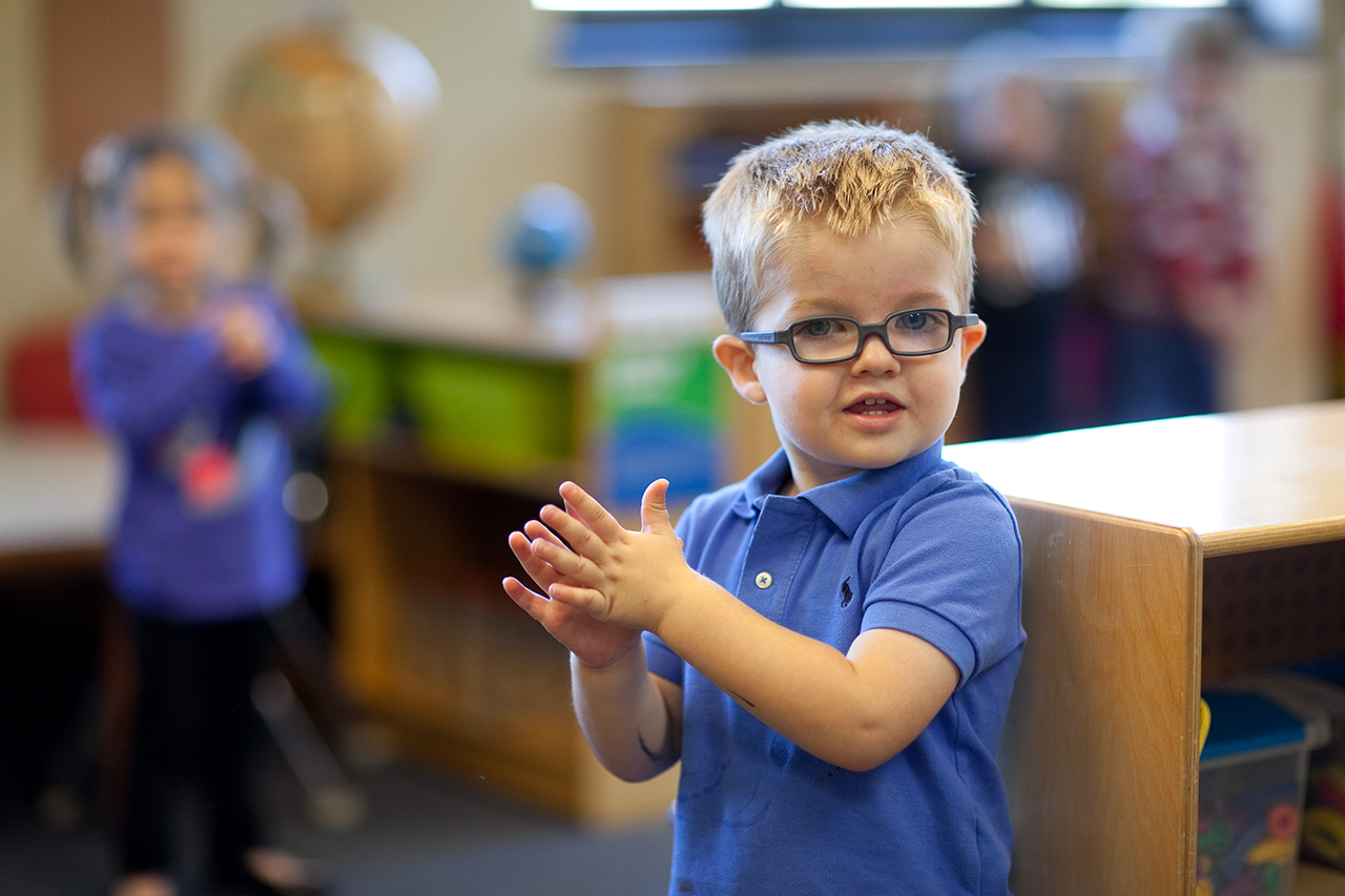 A young boy in a blue shirt claps his hands.