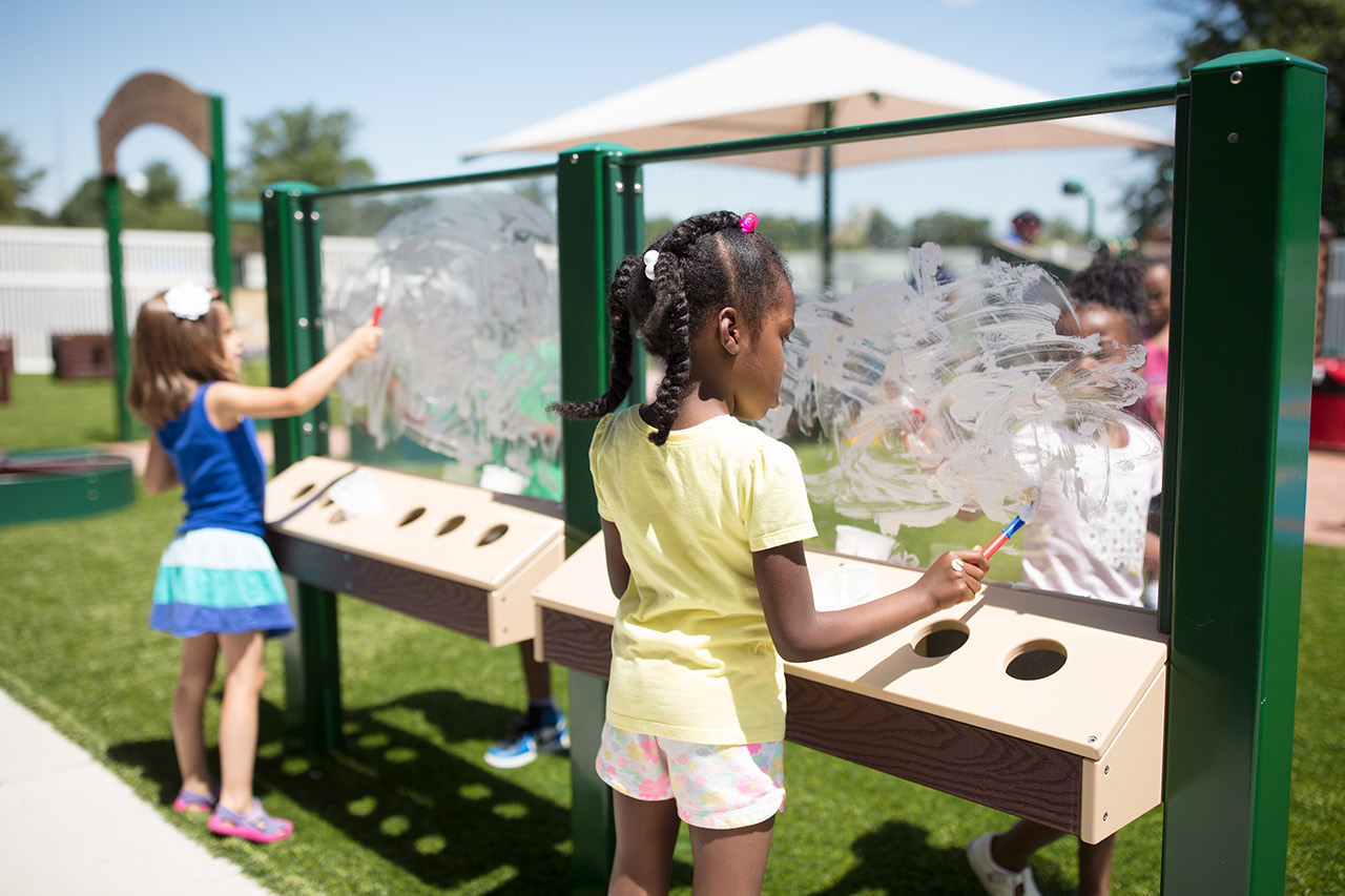 Four older girls paint at an outdoor activity station.