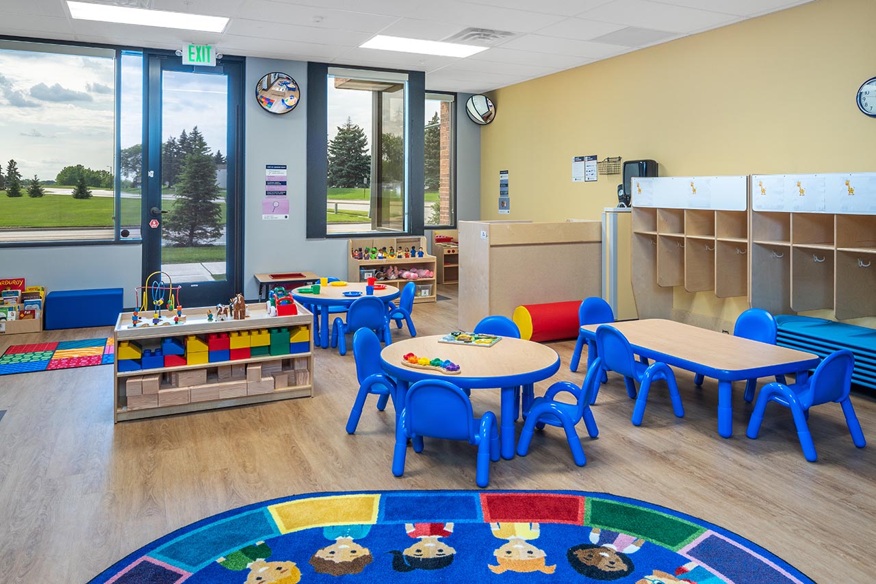 A Goddard School infant classroom with wooden cribs and large, colorful floor toys.