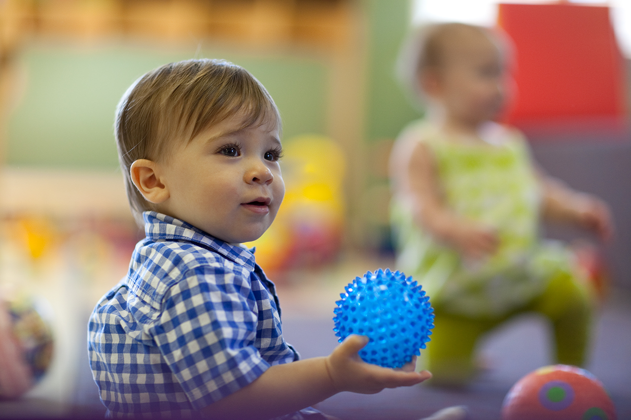 A young child in a checkered shirt holding a bright blue ball.