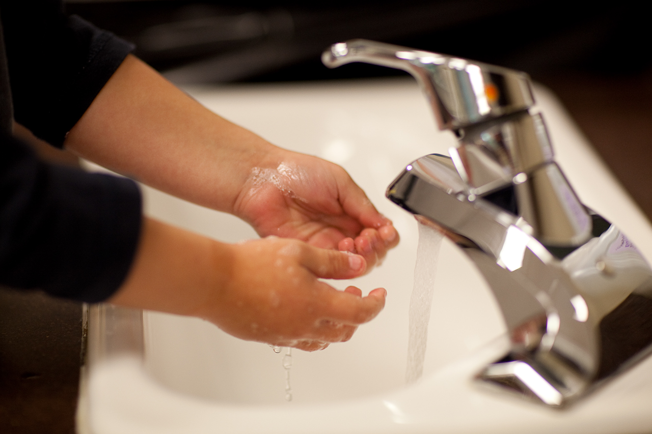 A child holding their soapy hands in front of a running faucet to wash them.